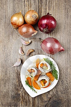 Pickled herring rolls with vegetables on wooden table