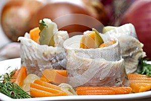 Pickled herring rolls with vegetables on wooden table