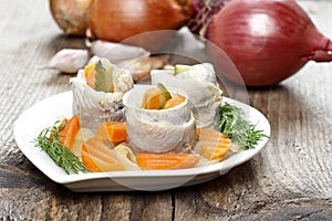 Pickled herring rolls with vegetables on wooden table