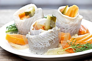 Pickled herring rolls with vegetables on wooden table