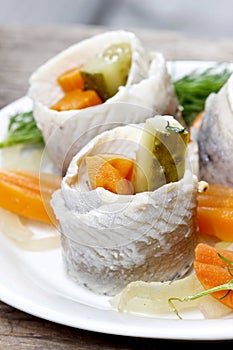 Pickled herring rolls with vegetables on wooden table