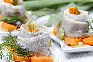 Pickled herring rolls with vegetables on wooden table