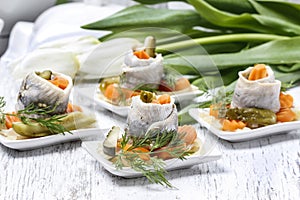 Pickled herring rolls with vegetables on wooden table