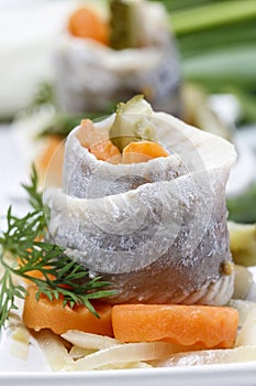 Pickled herring rolls with vegetables on wooden table