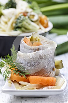 Pickled herring rolls with vegetables on wooden table