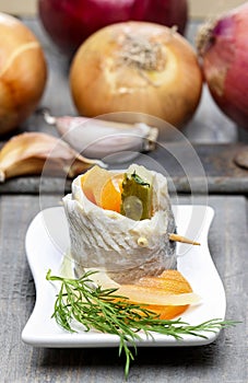 Pickled herring rolls with vegetables on wooden table