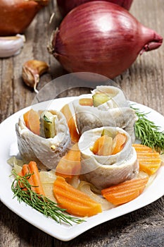 Pickled herring rolls with vegetables on wooden table