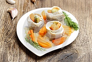 Pickled herring rolls with vegetables on wooden table