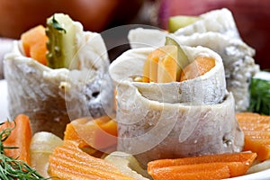 Pickled herring rolls with vegetables on wooden table