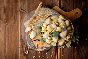 Pickled mushrooms in glass bowl with spices and dill on wooden table.