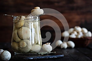 Pickled mushrooms in a glass jar on a dark background. Rustic still life