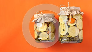 Pickled patissons and cucumbers in glass jars on a bright orange background, Top view, Copy space