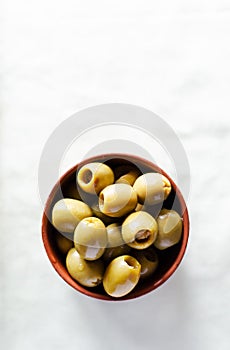 Pickled pitted green olives in a ceramic bowl on a light background. The concept of vegetarian food. Rustic style. Top view.