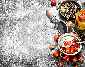 Pickled tomatoes in a bowl with spices and seamer.