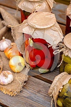 Pickled tomatoes and cucumbers in glass jars on an old wooden table. Summer harvest.