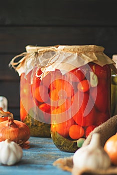 Pickled tomatoes in a glass jar on an old wooden table with a dark background