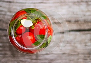Pickled tomatoes in a glass jar on an old wooden table. Summer harvest