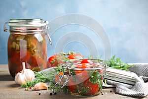 Pickled tomatoes in glass jars and products on table against blue background, space for text