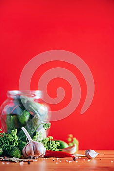 Pickling cucumbers in cans. Ingredients for marinated gherkins, glass jar, garlic, dill, salt, pepper on red background