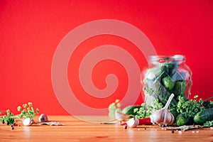 Pickling cucumbers in cans. Ingredients for marinated gherkins, glass jar, garlic, dill, salt, pepper on red background