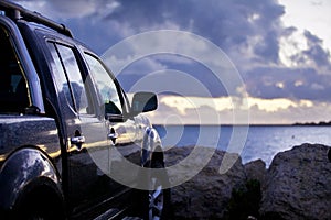 Pickup truck parked by sea with cloudy sunset