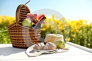 Picnic basket with bottle of wine and food on wooden table in lily field