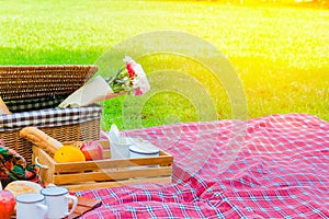 Picnic basket has a lot of food on green grass.There are milk ,apples ,oranges.