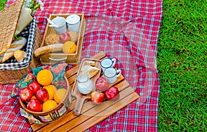 Picnic basket has a lot of food on green grass.There are milk ,apples ,oranges.