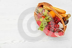Picnic basket with products and wine on white wooden table, top view