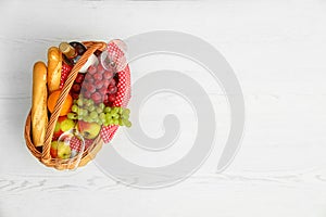 Picnic basket with products and wine on white wooden table, top view