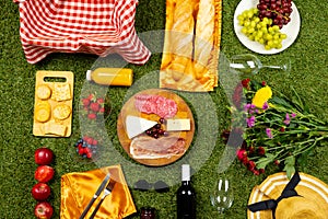 Picnic basket with vichy cloth and diverse food lying on green grass