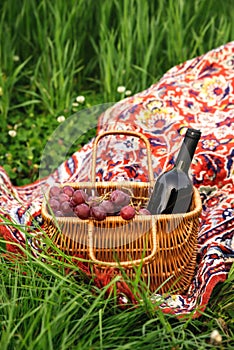 Picnic basket with wine bottle and grapes on green grass lawn.