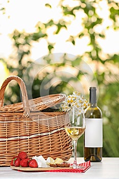 Picnic basket and wine with products on table against blurred background