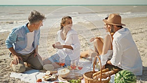 Picnic beach party friends enjoying casual conversation, drinking wine and tasting meal