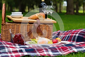 picnic blanket and basket overflowing with fresh fruit, cheese, and wine in a park setting