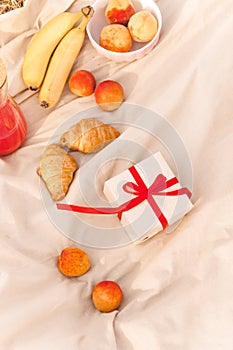 Picnic concept. Fruits, gift box, French croissants pastries, peaches and bananas on the bedspread.