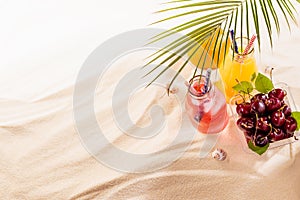 Picnic with food and drink on tropical beach, vacation background - fresh cold drinks with straw in glass bottles, green palm leaf