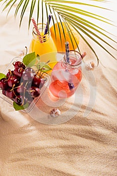 Picnic with food and drink on tropical beach, vacation background - fresh cold drinks with straw in glass bottles, green palm leaf