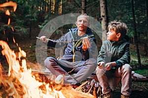 Picnic in forest - father and son roste marshmallow on campfire
