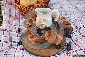 Picnic on the grass. Rustic milk in jug, cherry and delicious buns on a picnic. Closeup