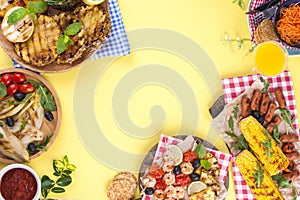 Picnic with grilled food. Sausages and corn on barbecue, shrimp, vegetables and fruits. Delicious summer lunch and plastic dishes.