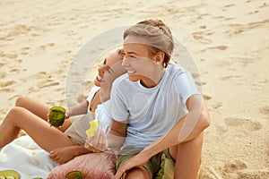 Picnic. Mother And Son Having Lunch On Beach. Young Woman And Handsome Boy Enjoying Organic Fruit And Looking Away.