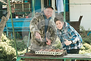 Picnic in nature. A man and his son are grilling marinated kebabs, spinning a skewer with their hands.