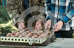 Picnic in nature. A man and his son are grilling marinated kebabs, spinning a skewer with their hands.