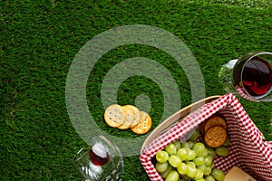 Picnic and relaxation, picnic basket, glass with red wine and grapes and snacks. Top view on the grass with space for advertising