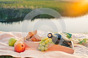 Picnic by the river. On a light-colored bedspread, a wooden tray with fruit,