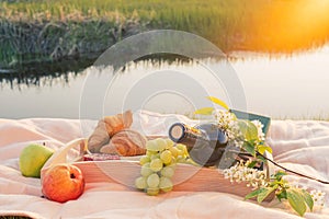 Picnic by the river. On a light-colored bedspread, a wooden tray with fruit,