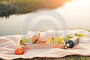 Picnic by the river. On a light-colored bedspread, a wooden tray with fruit,