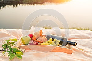 Picnic by the river. On a light-colored bedspread, a wooden tray with fruit,