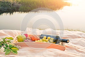 Picnic by the river. On a light-colored bedspread, a wooden tray with fruit,